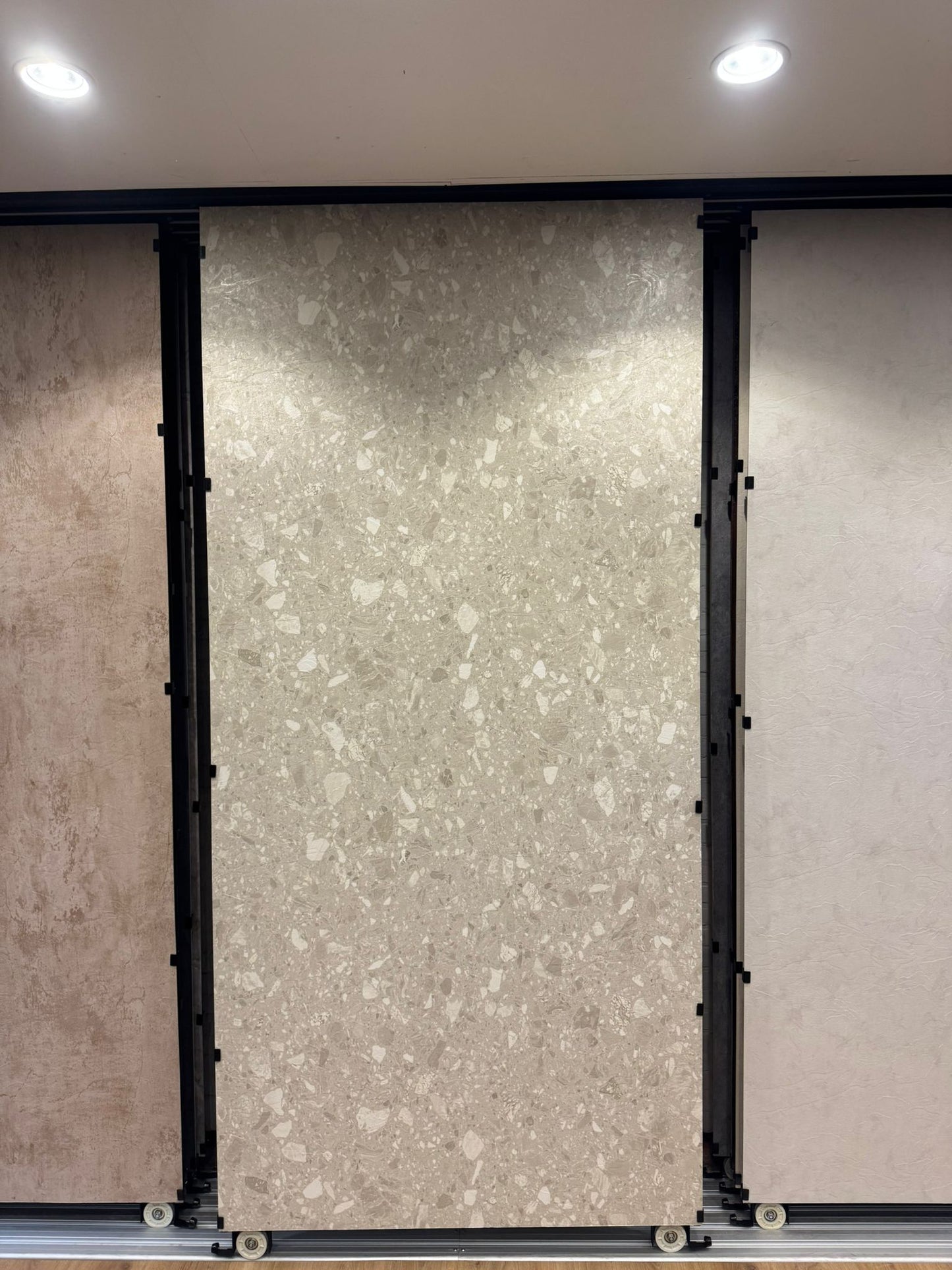 Beige terrazzo SPC wandpaneel in showroom opstelling met grote plaat en lichte steenkorrels