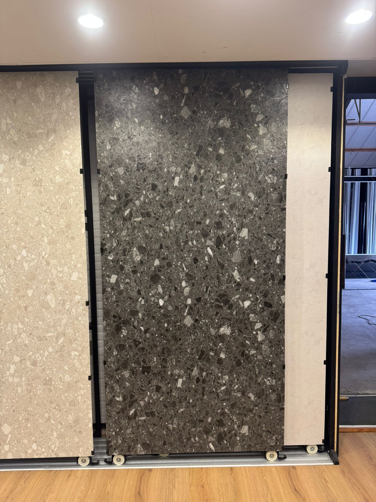 Donkergrijs terrazzo SPC wandpaneel in showroom opstelling met grote plaat en grove steenkorrels