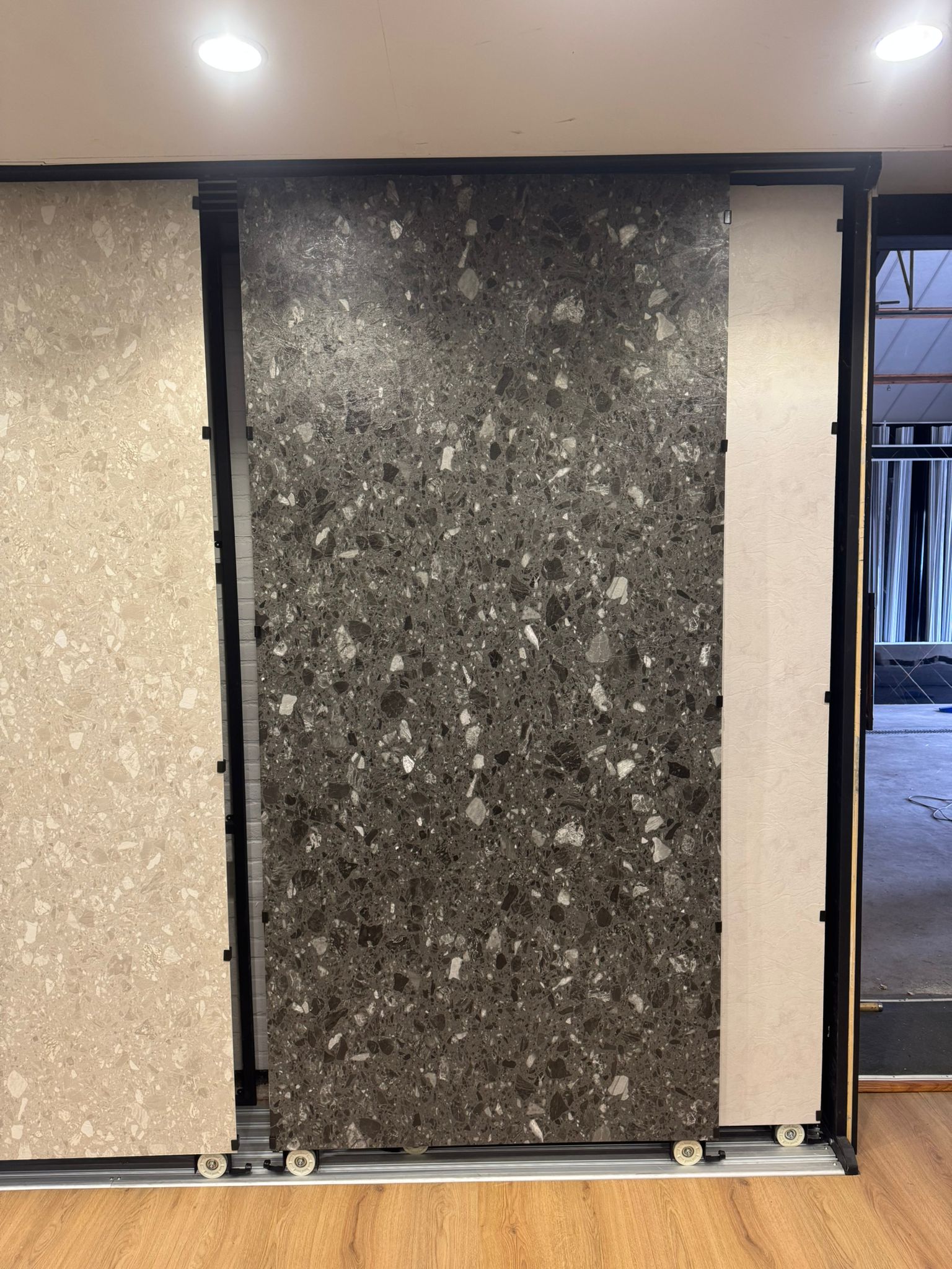 Donkergrijs terrazzo SPC wandpaneel in showroom opstelling met grote plaat en grove steenkorrels