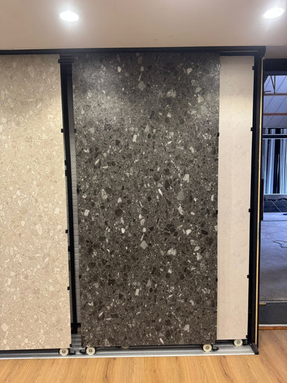 Donkergrijs terrazzo SPC wandpaneel in showroom opstelling met grote plaat en grove steenkorrels