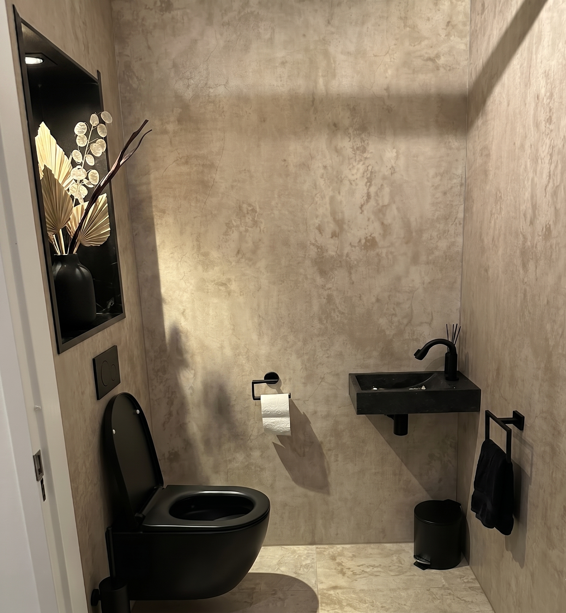 Modern toilet met beige betonlook SPC wandpanelen, zwarte hangtoilet en compacte wastafel voor een strakke en luxe uitstraling